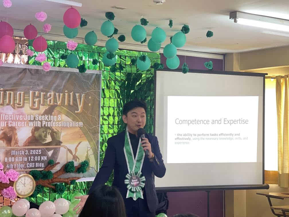 Jayson Ryan Co speaking with a microphone beside a slide titled Competence and Expertise at Baliuag University