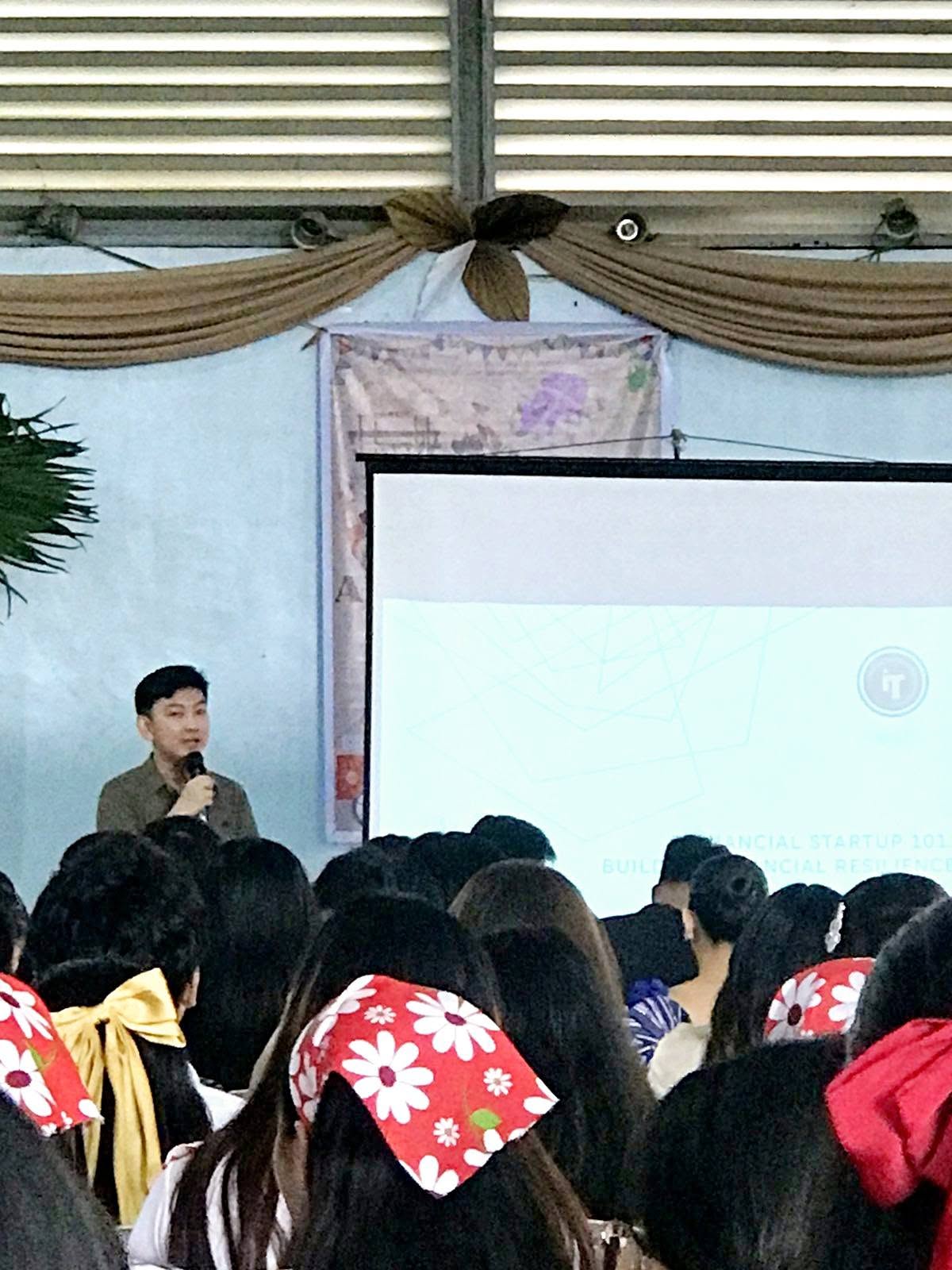 Jayson speaking with a microphone on stage during Finance Talk 101 at the College of Mary Immaculate