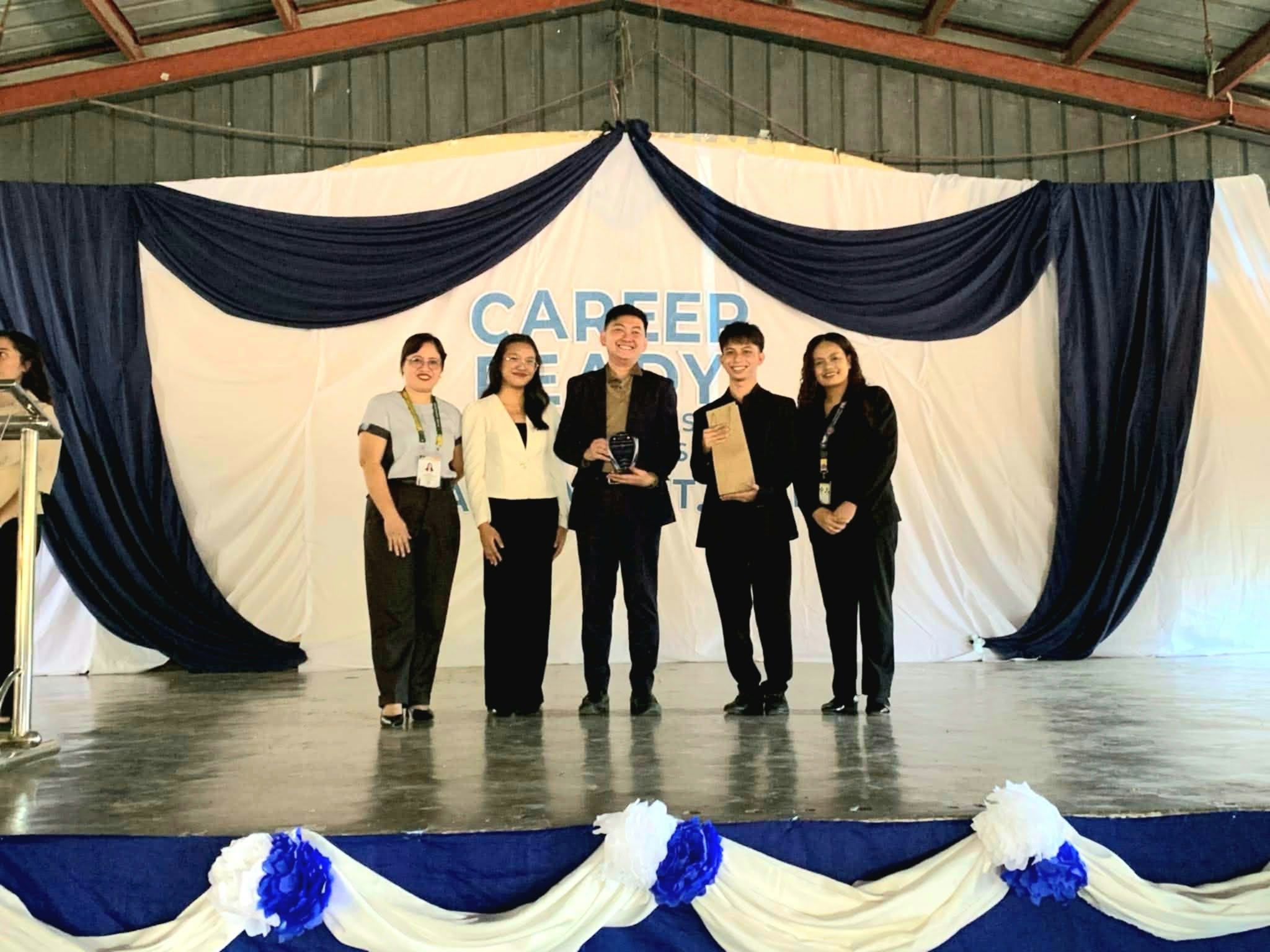 Jayson holding his plaque of appreciation on stage with CvSU faculty and student organizers