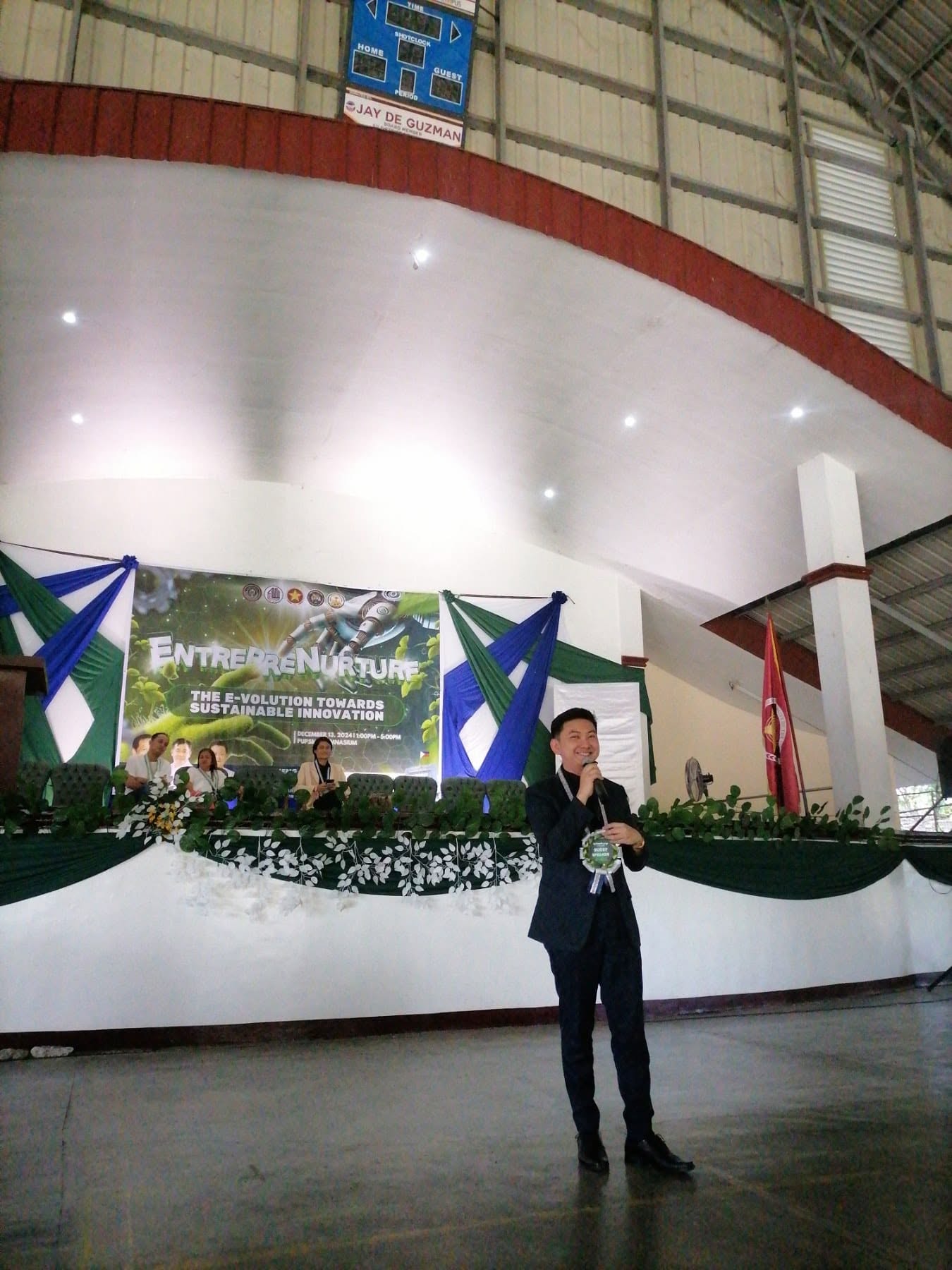 Jayson addressing the audience in front of the EntrepreNurture stage and banner