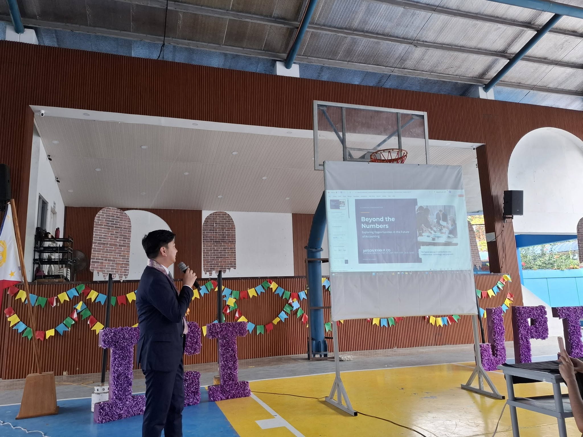 Jayson Ryan Co speaking with a microphone beside a projected slide titled Beyond the Numbers: Exploring Opportunities in the Future of Accounting